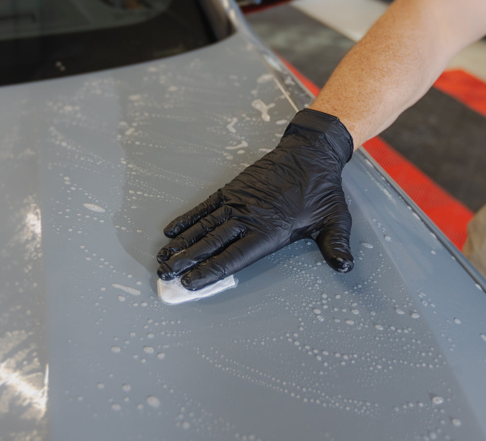 Clay bar being moved by hand over lubricated paintwork